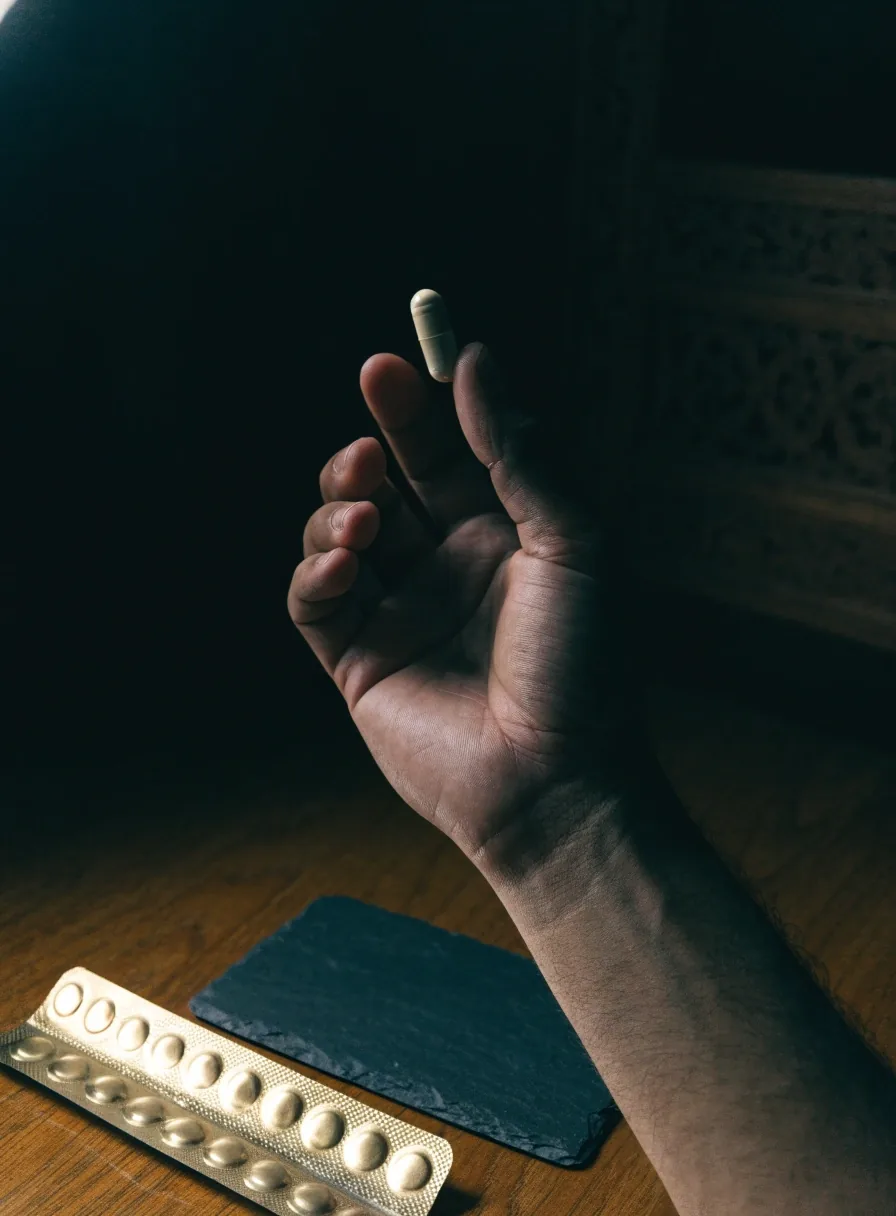 A hand holding a matte capsule over a dark slate plate beside an unprinted blister strip
